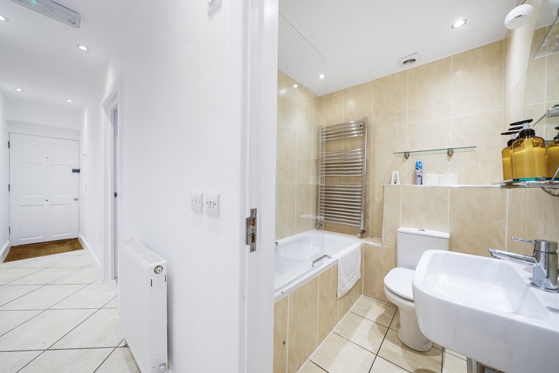 Modern bathroom with beige tile walls, white sink, toilet, bathtub and heated towel rail