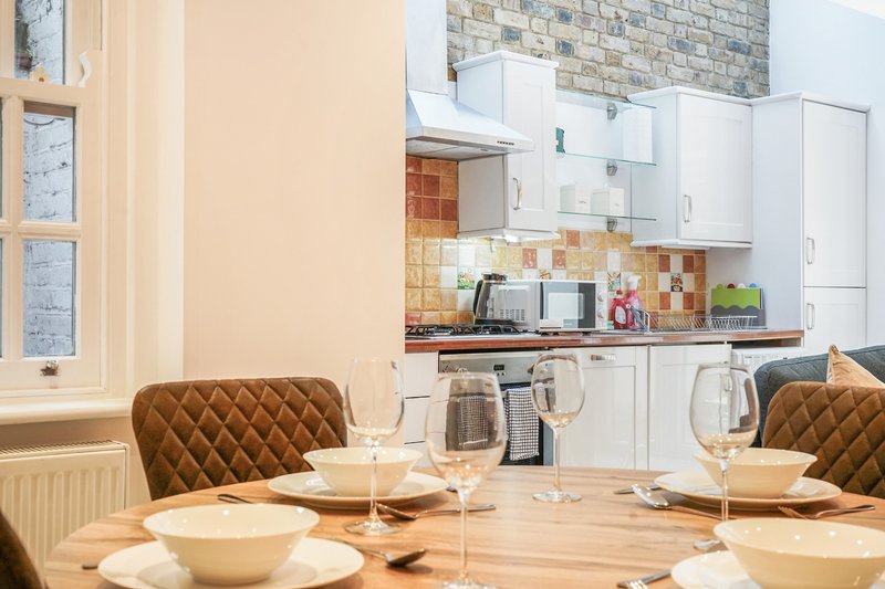 Modern kitchen diner with white cabinetry, wooden table, brown quilted chairs and place settings