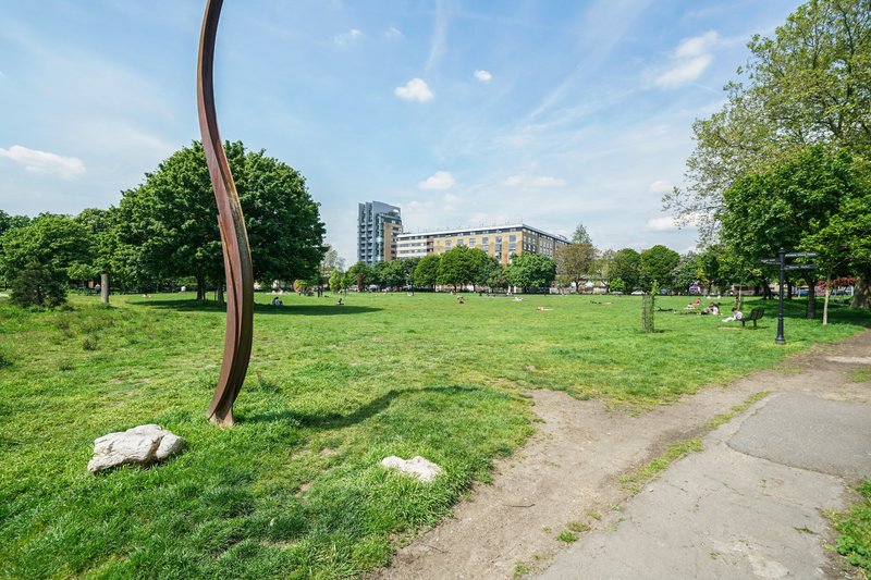 Public park with green lawn, curved metal sculpture, pathway and residential buildings in distance