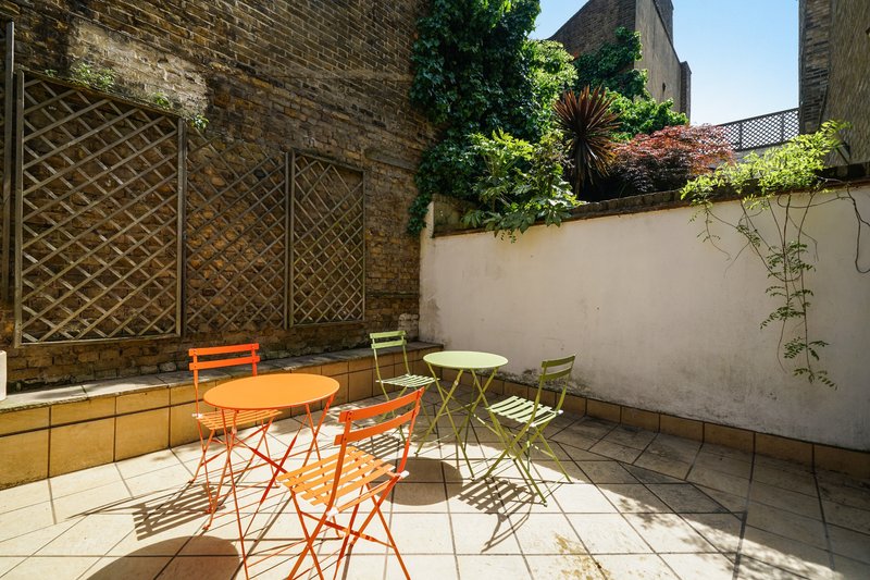 Sunny courtyard patio with orange and green metal chairs, round tables, and climbing ivy on stone walls