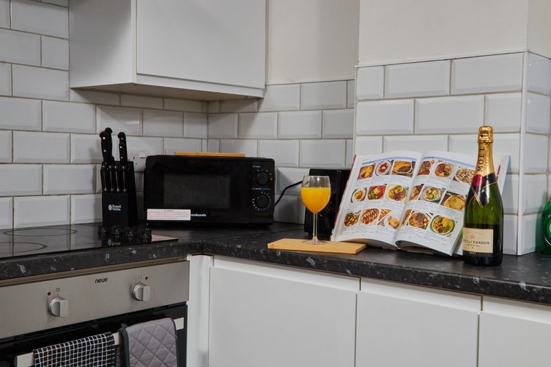 Modern kitchen with white subway tile backsplash, black countertop, microwave, knife block, and champagne bottle