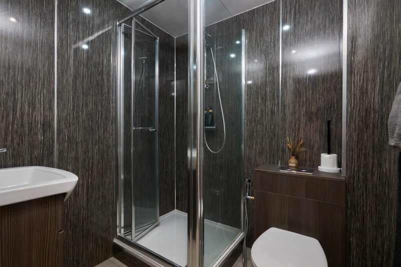 Modern bathroom with dark wood-grain tiles, glass shower enclosure, white toilet and sink
