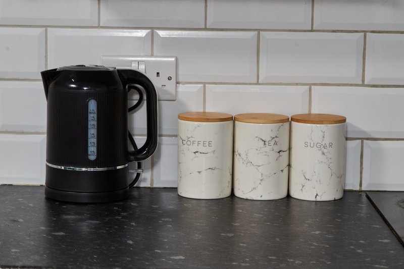 Kitchen counter with black electric kettle and three ceramic storage jars labeled coffee, tea, and sugar