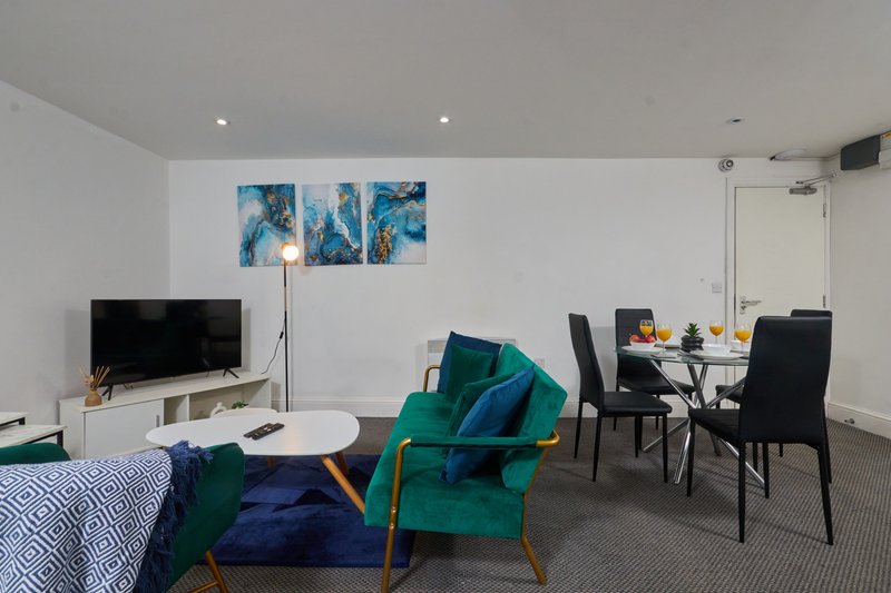 Modern open-plan living space with green armchair, dining table, TV, and blue abstract wall art