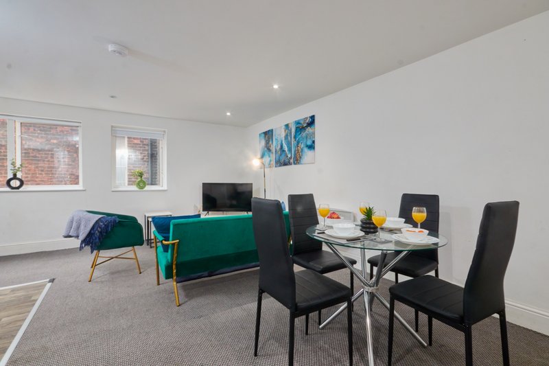 Open-plan living and dining area with teal sofa, dining table, black chairs and windows