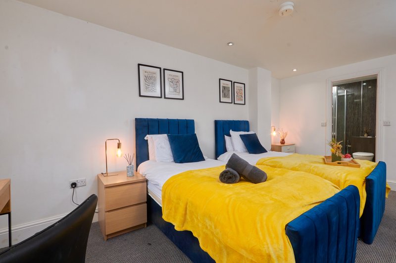 Modern bedroom with two single beds, blue headboards, yellow bedding, wooden nightstands and wall art