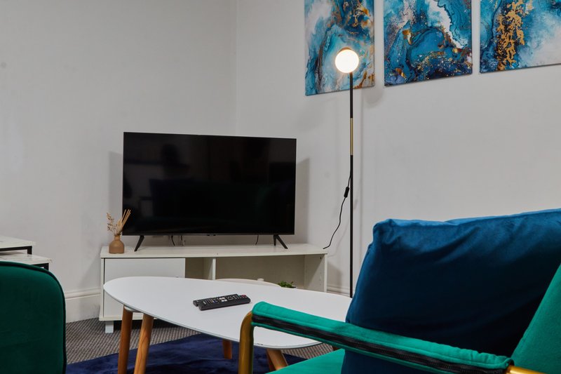 Living room with TV on white stand, green armchair, blue cushion, floor lamp and wall art