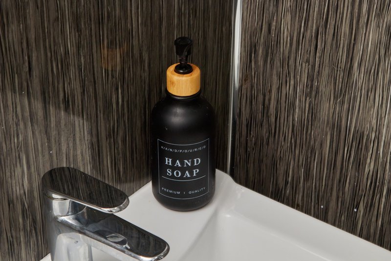 Bathroom sink with black hand soap dispenser and chrome soap dish against striped tile wall
