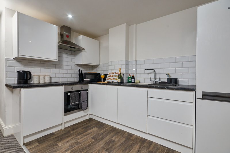 Modern kitchen with white cabinetry, black countertops, subway tile backsplash and wooden flooring