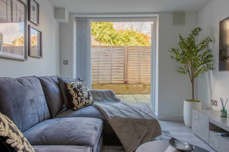 Modern living room with blue sofa, potted plant, framed wall art and glass doors to garden