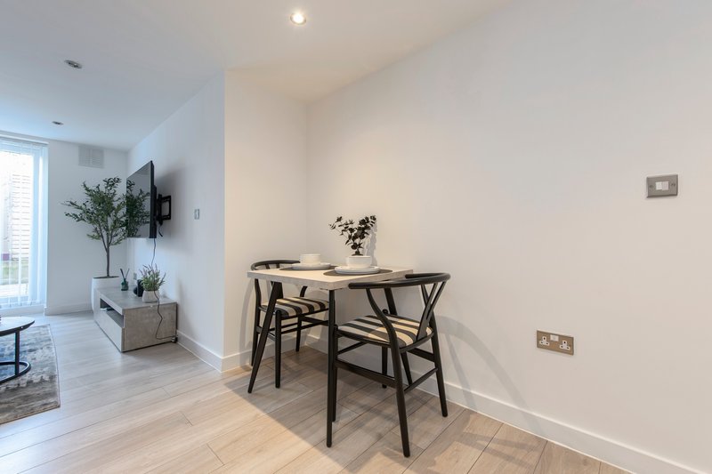Modern dining area with black table, wishbone chairs, potted plant and wall-mounted TV