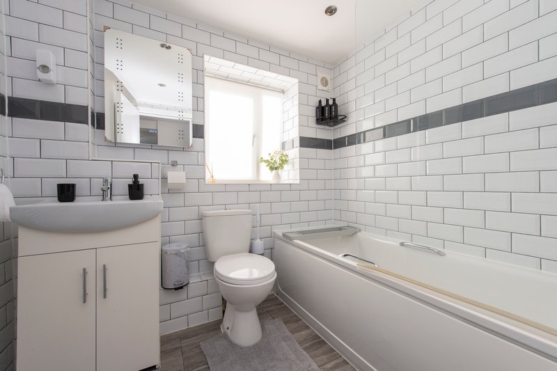 Modern bathroom with white subway tiles, vanity sink, toilet, bathtub and window