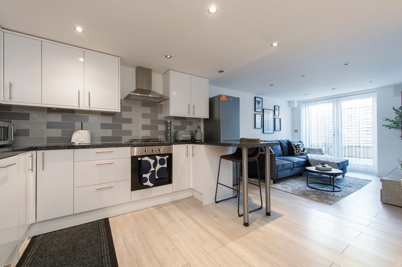 Open-plan kitchen and living area with white cabinetry, grey tile splashback, wooden flooring and blue sofa