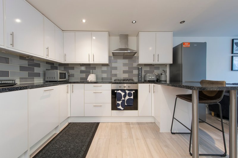 Modern kitchen with white cabinetry, gray tile backsplash, stainless steel appliances and wooden flooring