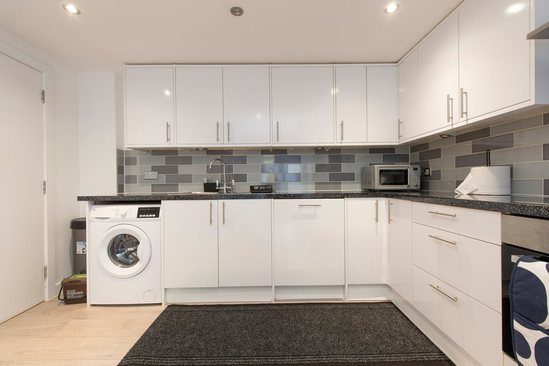Modern kitchen with white cabinetry, black worktops, tiled backsplash, washing machine and appliances