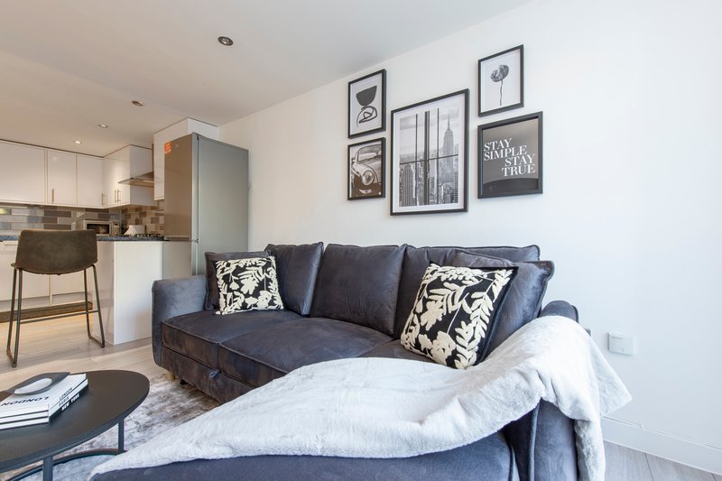 Open-plan living area with navy sofa, white bedding, kitchen, and framed wall art