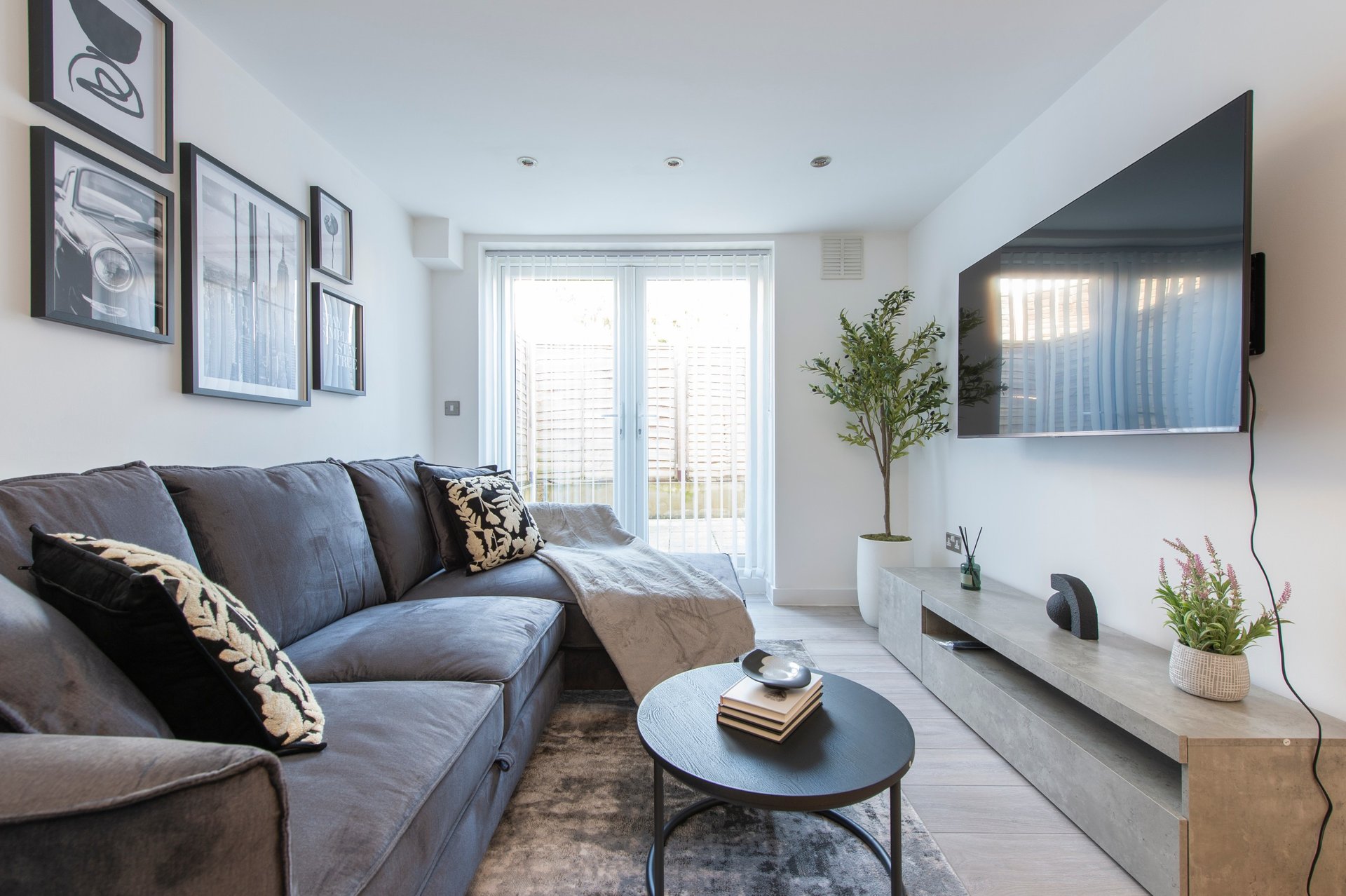 Modern living room with grey sofa, TV, coffee table, and patio doors to garden