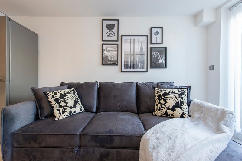 Living room with dark grey corner sofa, patterned cushions, sheepskin throw, and framed wall art