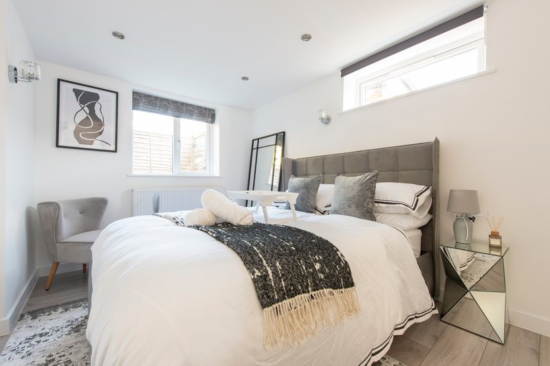 Modern bedroom with double bed, grey headboard, white bedding, and framed wall art