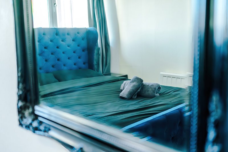 Modern bedroom with teal four-poster bed, striped bedding, decorative pillows and sheer curtains