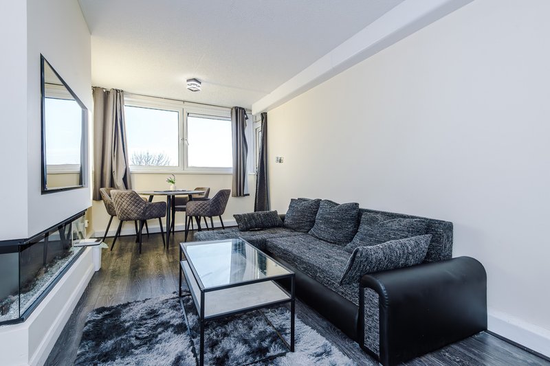 Modern living room with grey sofa, dining table, large windows and fireplace