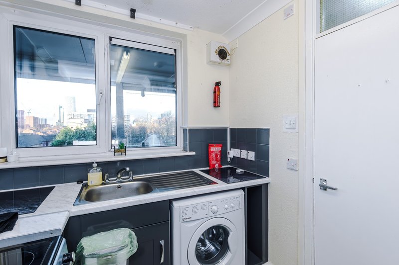 Modern kitchen with dark cabinetry, sink, washing machine, and city view from window