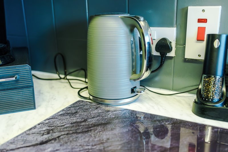 Kitchen countertop with kettle, toaster, and electrical outlets on tiled wall