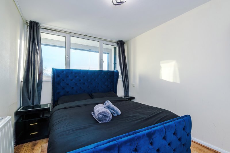 Modern bedroom with blue upholstered bed, black bedding, dark curtains and window view
