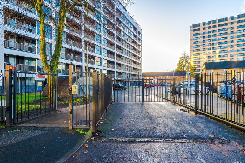 Modern apartment building exterior with gated courtyard, parking area and surrounding residential complex