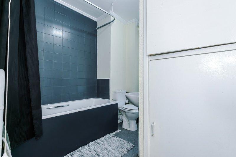 Modern bathroom with dark blue tile shower bath, white toilet, and light gray bath mat