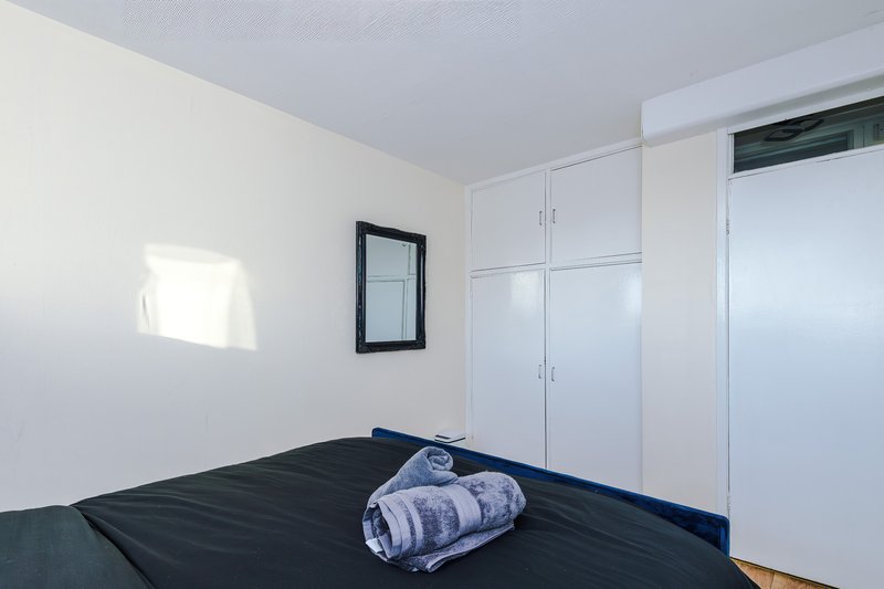 Minimalist bedroom with black bed, white built-in wardrobe and small framed mirror