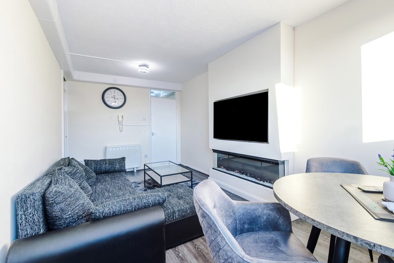 Modern living room with grey sofa, wall-mounted TV, dining table and clock