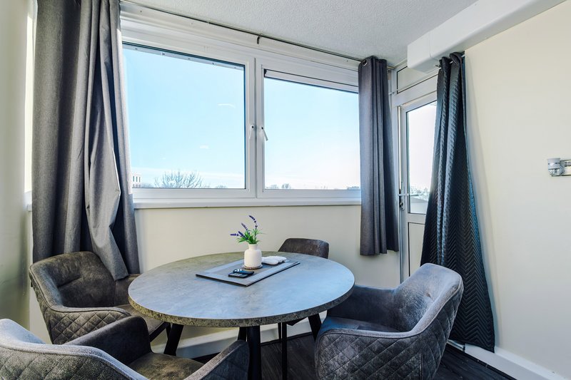 Bright dining nook with round table, upholstered chairs, large windows and blue curtains