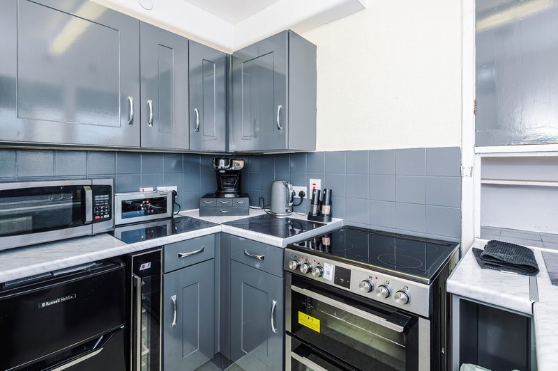 Modern kitchen with grey cabinets, black appliances, tiled splashback and countertop