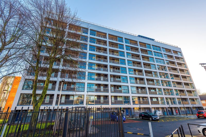 Modern multi-storey apartment building with blue and brown facade, bare trees and parking area