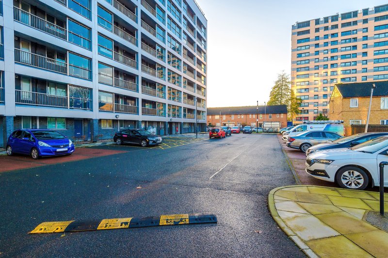 Modern apartment building exterior with parking area, multiple vehicles and surrounding residential buildings