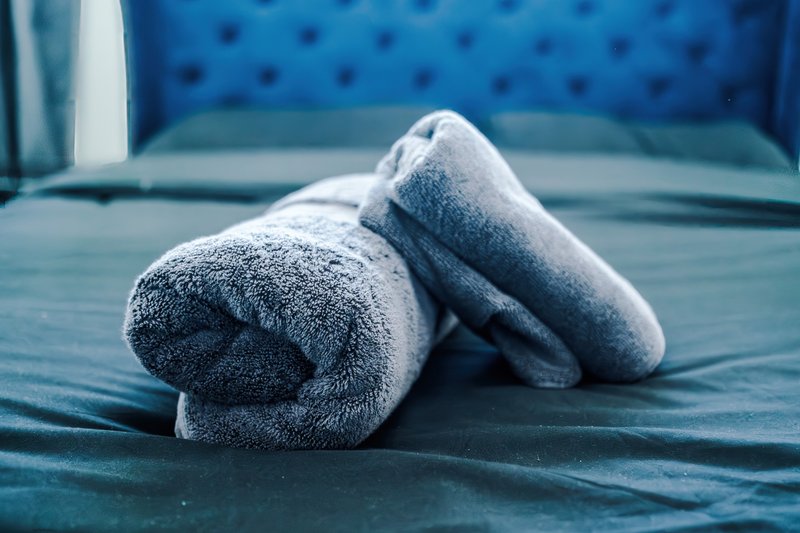 Rolled grey towels on blue bedding with upholstered headboard
