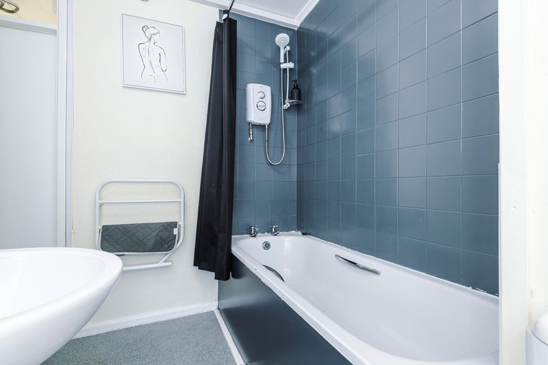 Modern bathroom with white toilet, blue-tiled shower enclosure, white bathtub and black shower curtain
