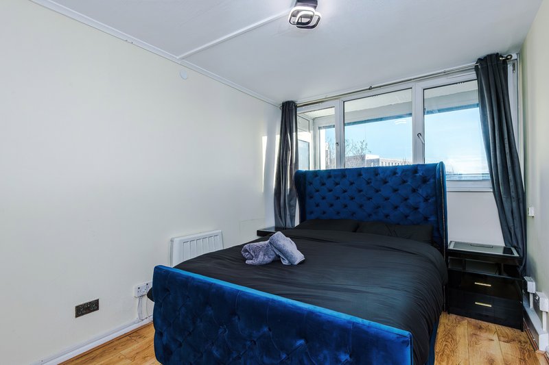 Bedroom with blue upholstered bed, wooden floor, large window with city view