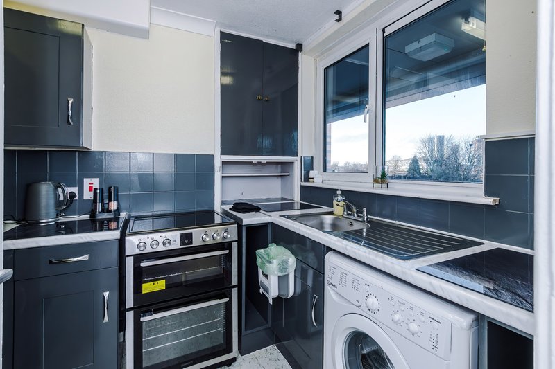 Modern kitchen with dark cabinetry, built-in oven, hob, sink, and washing machine
