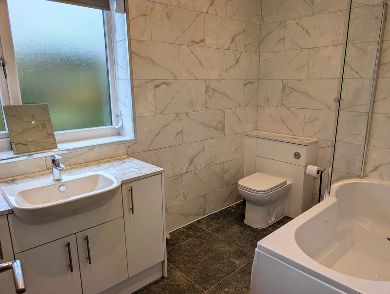 A bright, modern bathroom with a full-size bath with shower, WC and wash basin, providing a practical and comfortable space for groups and contractors.