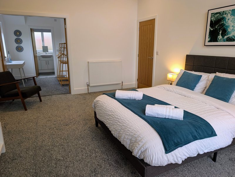 A bright, spacious king-size bedroom with a comfortable bed. The room also features a cosy seating area and direct access to the ensuite and dressing area.