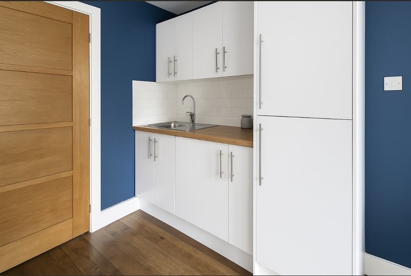 Modern kitchenette with white cabinets, wooden worktop, blue walls and wooden flooring
