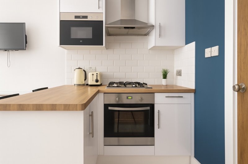 Modern compact kitchen with white cabinetry, wooden worktop, gas hob and stainless steel appliances