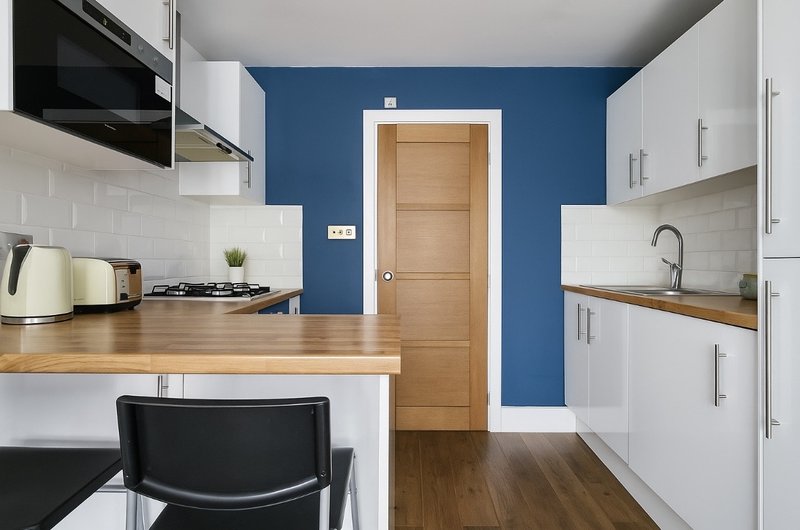 Modern kitchen with white cabinetry, blue accent wall, wooden countertop and black chair