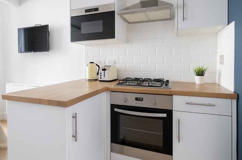 Modern kitchen with white cabinetry, wooden countertop, gas cooktop, built-in oven and microwave