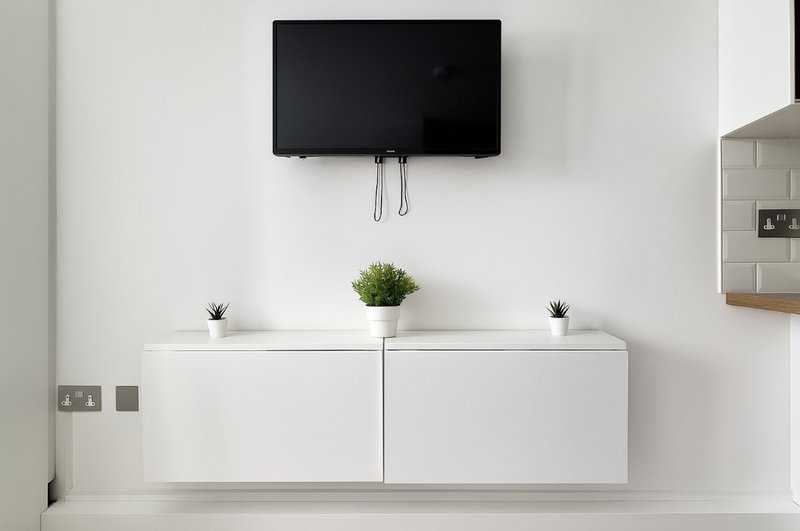Modern living room with wall-mounted TV, white storage cabinet, and potted plant