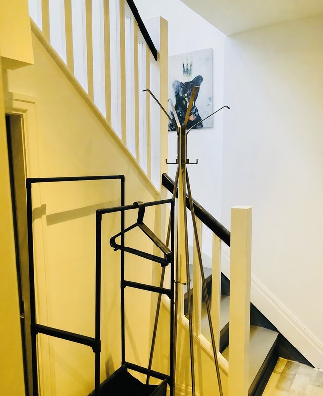 Bright stairwell with yellow walls, white railings, coat stand and framed artwork