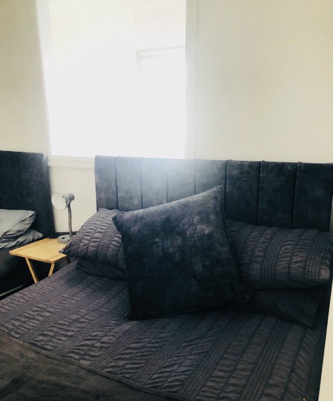 Bedroom with dark upholstered bed, geometric patterned bedding, cushions and small side table