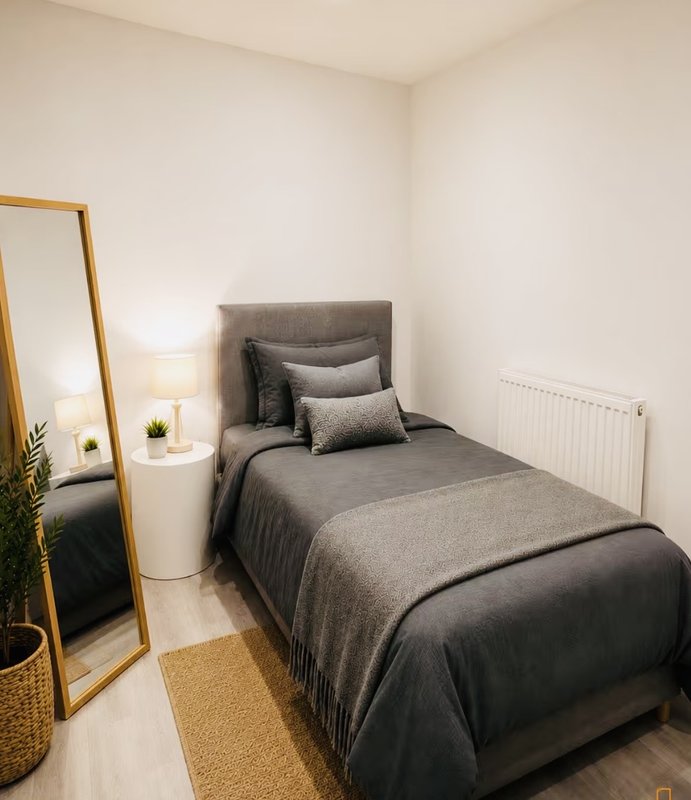 Bedroom with single bed, gray bedding, standing mirror, radiator and white walls